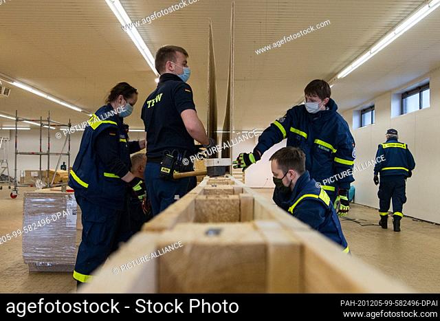 05 December 2020, Wilhelmshaven: THW workers assemble partition walls made of chipboard panels during the construction of a vaccination centre in an empty...