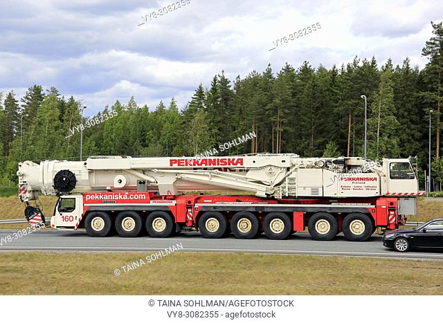 Side view of large Liebherr 8-axle mobile crane of Pekkaniska at speed on road with an overtaking car. Salo, Finland - June 8, 2018