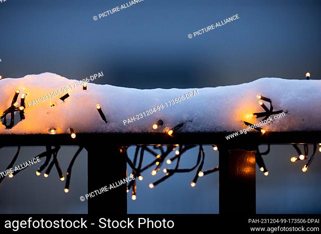04 December 2023, North Rhine-Westphalia, Cologne: Snow lies on a chain of lights on a balcony railing. Photo: Rolf Vennenbernd/dpa