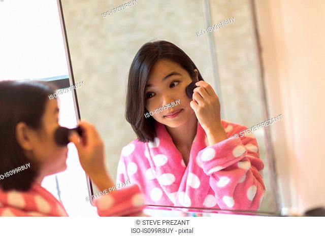 Young woman applying makeup using bathroom mirror