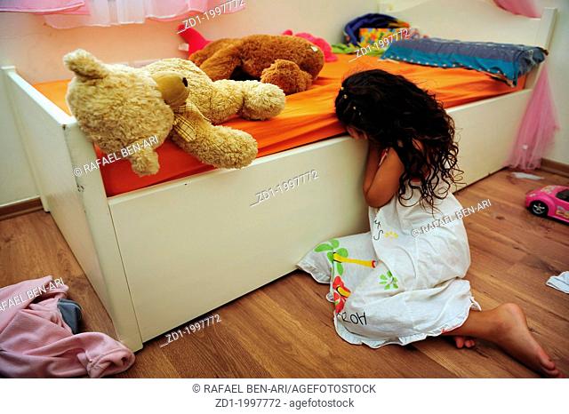 A young girl who is a victim of domestic violence cries on the floor of her bedroom