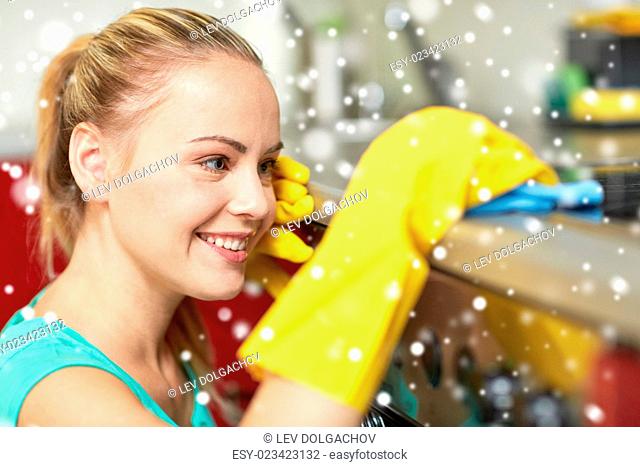 people, housework and housekeeping concept - happy woman cleaning cooker at home kitchen over snow effect