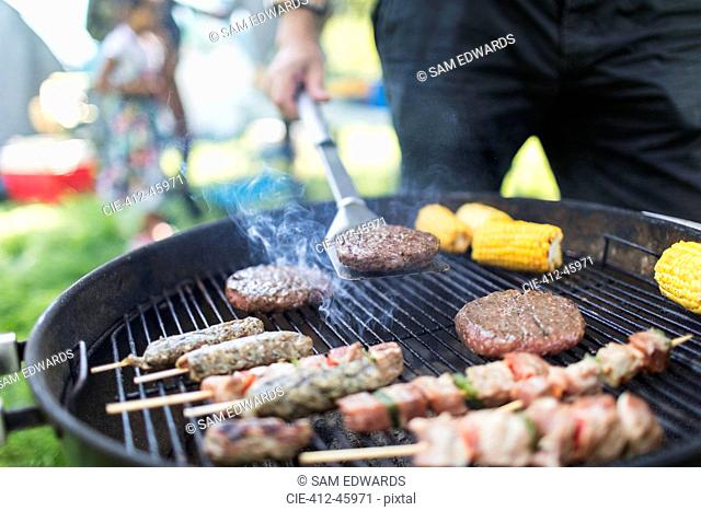 Man barbecuing hamburgers, kebabs and corn cobs
