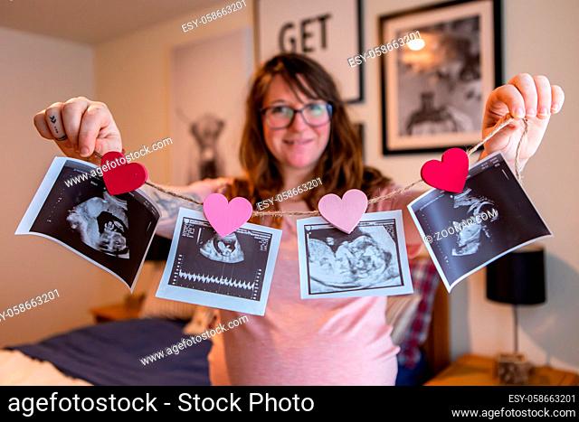 A selective focus view of a happy expectant mother showing four echography, ultrasound, baby scans at different trimesters of pregnancy, with hearts