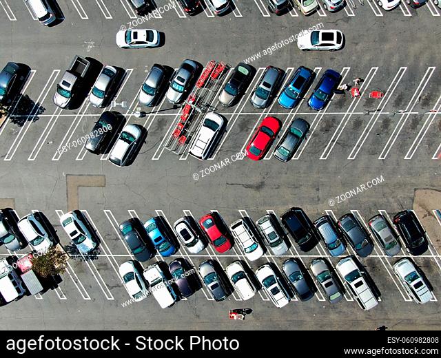 Aerial top view of parking lot at shopping mall with varieties of colored vehicles. People walking to their car and trying to park
