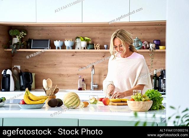 Attratctive middle age woman cutting fruit in her kitchen