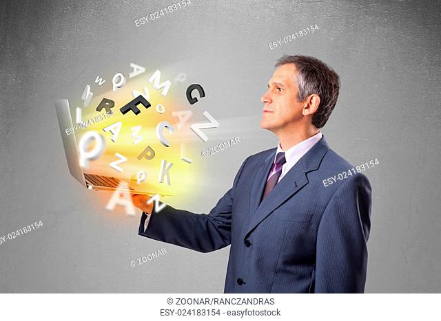Middle aged businessman holding laptop with colorful letters