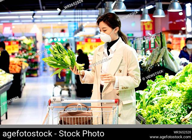 Wearing a mask of the young woman picking vegetables in the supermarket