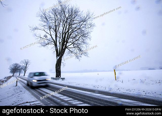 06 December 2023, Mecklenburg-Western Pomerania, Groß Strömkendorf: A car drives over a snow-covered road. (Shot with long exposure time) Persistent snowfall...