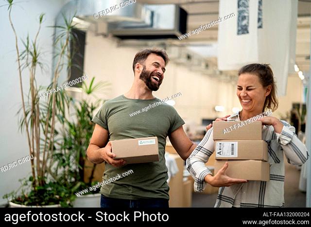 Two coworkers having fun while carrying cardboard boxes