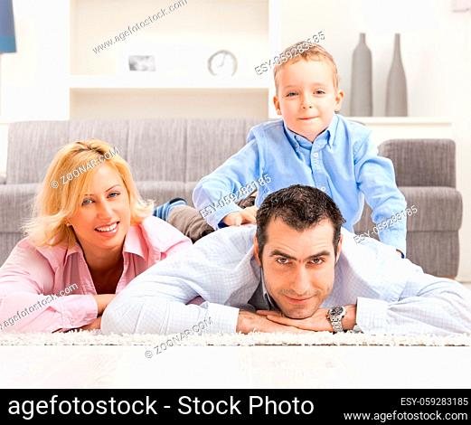 Happy couple and their son lying together on carpet in living room