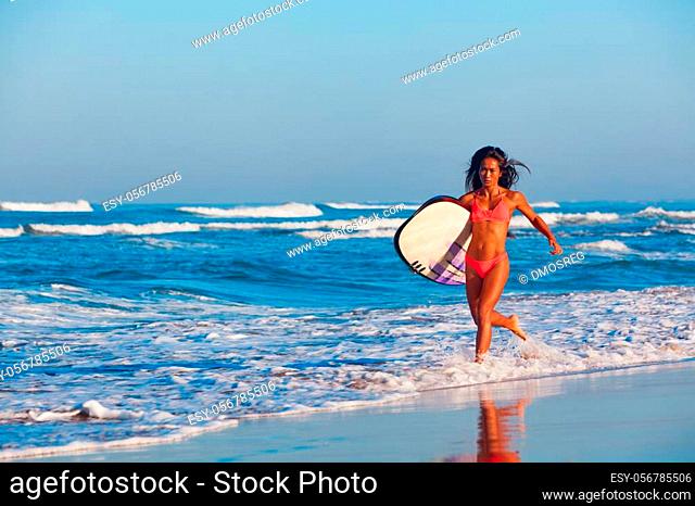 Girl in bikini with surf board has fun. Woman surfer run into water, jump with splashes through ocean wave. People in water sport adventure camp