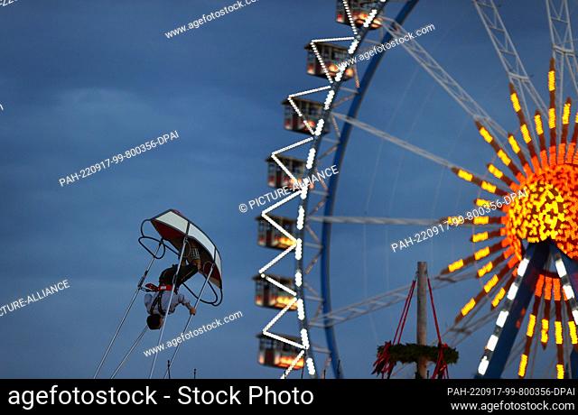 17 September 2022, Bavaria, Munich: A young man is swinging in the boat swing in front of the Ferris wheel at dusk. Photo: Karl-Josef Hildenbrand/dpa