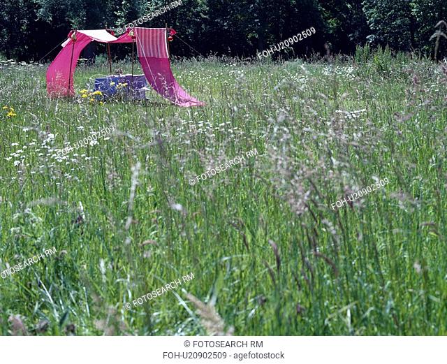 Pink cotton awning in field of long grass in country garden in summer