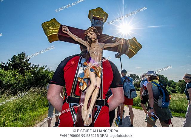 06 June 2019, Bavaria, Regensburg: A pilgrim carries a wooden cross during the largest pilgrimage on foot in Germany. Until Saturday