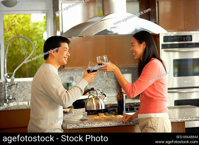 Young couple clinking glasses of red wine in kitchen