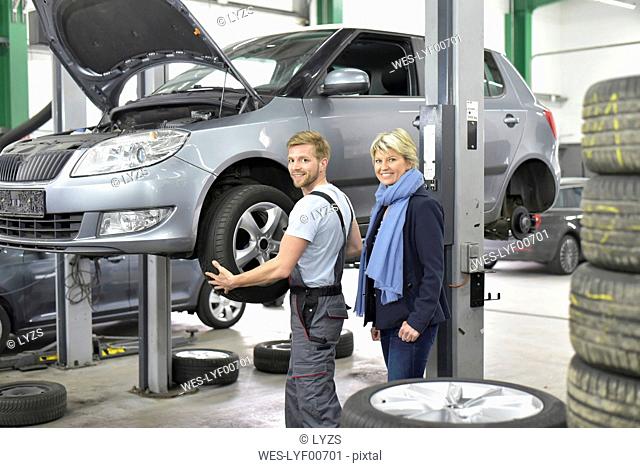 Portrait of smiling car mechanic with client in workshop at car