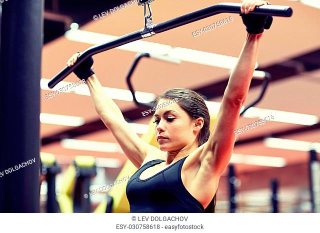 sport, fitness, bodybuilding, lifestyle and people concept - woman flexing arm muscles on cable machine in gym