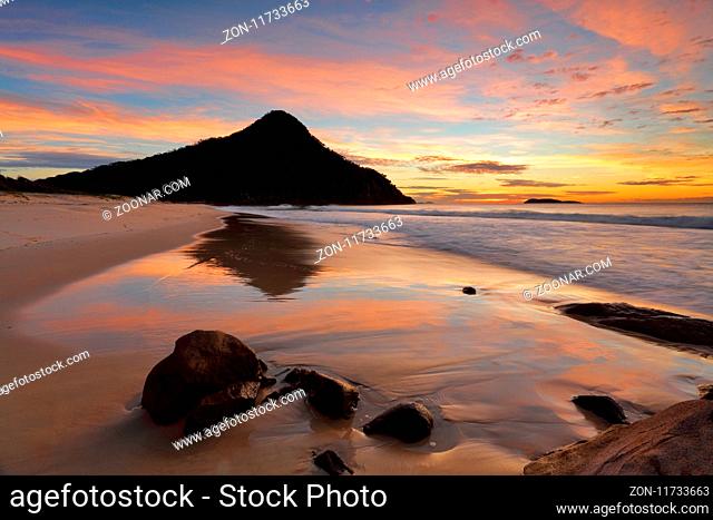 Zenith Beach and reflections in the shorebreak  Mt Tomaree and Boondelbah island in silhouette against the beautiful dawn sunrise light illuminating the sky