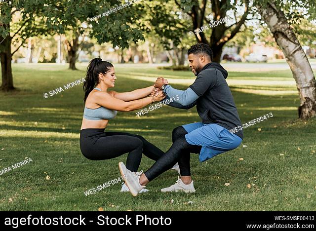 Couple holding hands while doing crouching exercise together at backyard