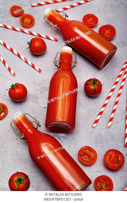 Homemade tomato juice in swing top bottles, straws and tomatoes on grey ground