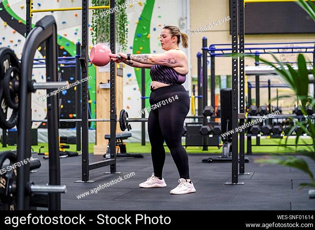Young overweight woman working out with kettlebell in gym