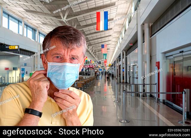 Senior man or traveler adjusting face mask in airport terminal and looking afraid of travel with coronavirus