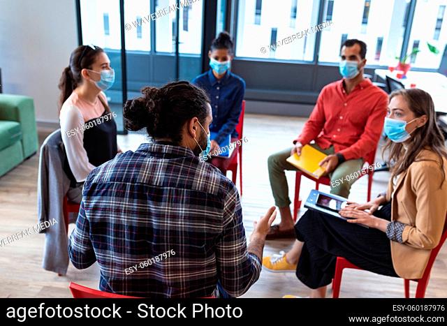 Diverse group of creative colleagues wearing face masks talking at meeting