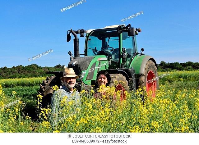 couple of farmers in a canola field with a tractor.Porqueres, Girona, Catalonia, Spain