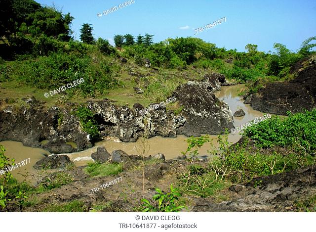 Small muddy river cuts its way through a thick layer of black pyroclastic debris from the volcano Gunung Rinjani iin a small rugged gorge Batu Nampar Lombok...