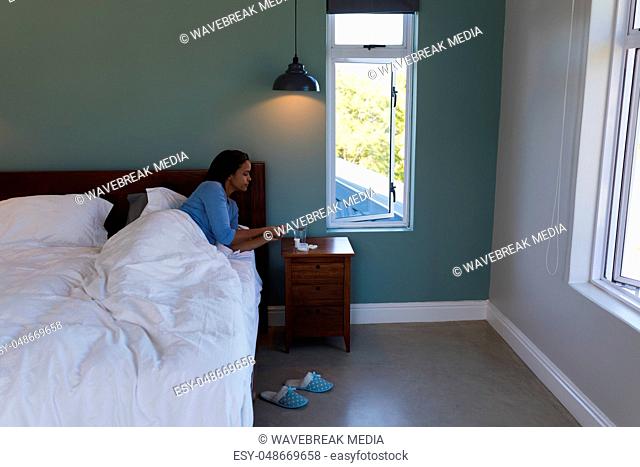 Senior woman taking medicine with glass of water while lying in bed at home