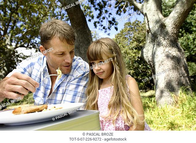 Close-up of a girl sitting with her father at a picnic table