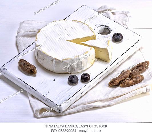 round Camembert cheese on a white wooden board, white wooden table, top view