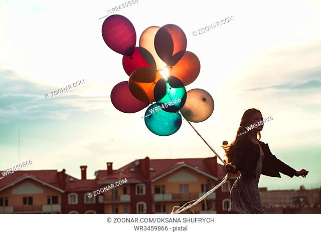 Pretty girl with big colorful balloons walking on the hills near the town. Focus on balloons