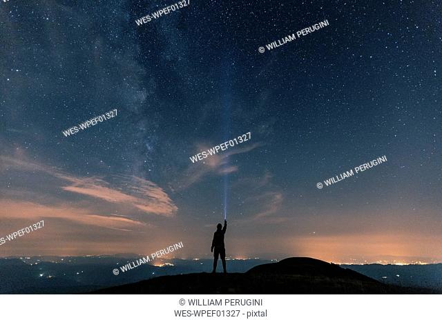 Italy, Monte Nerone, silhouette of a man with torch under night sky with stars and milky way