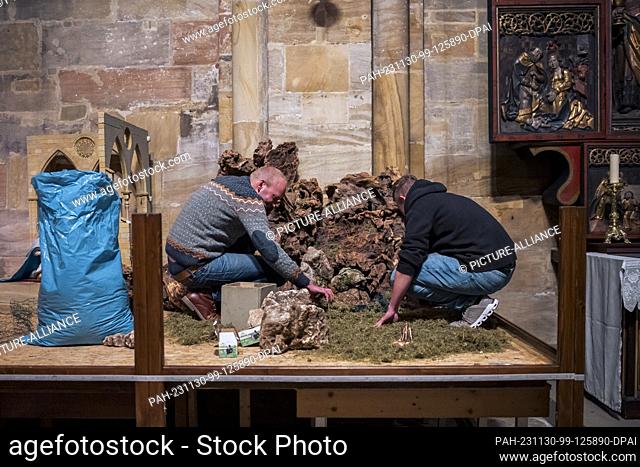 PRODUCTION - 29 November 2023, Bavaria, Bamberg: Andreas Tolle (l) and Marco Saffer (r) cover the floor of the nativity scene with moss