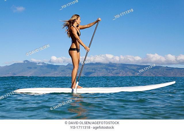 Fit, athletic woman stand up paddles at Napili Bay, Maui, Hawaii with Molokai in the distance