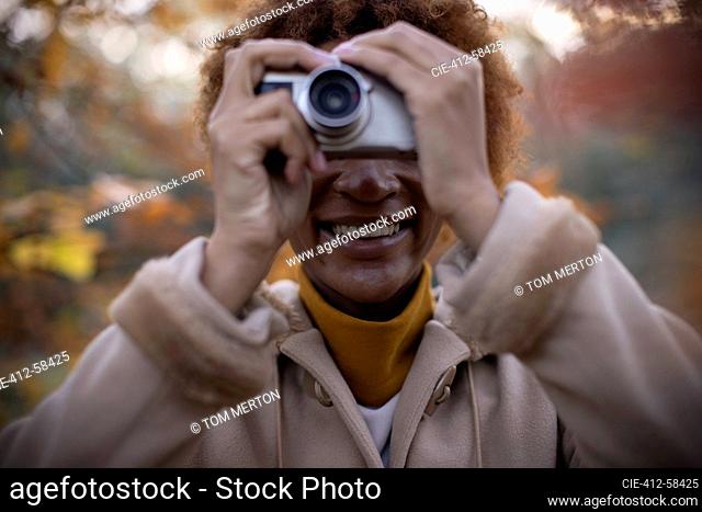 Happy young woman using digital camera in autumn park
