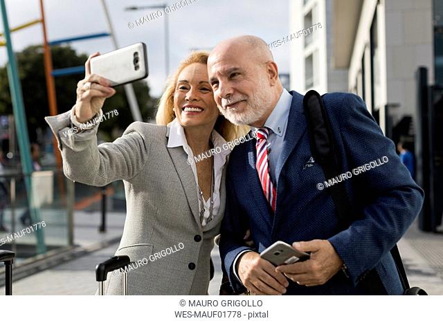 Senior businessman and businesswoman with baggage taking a selfie in the city