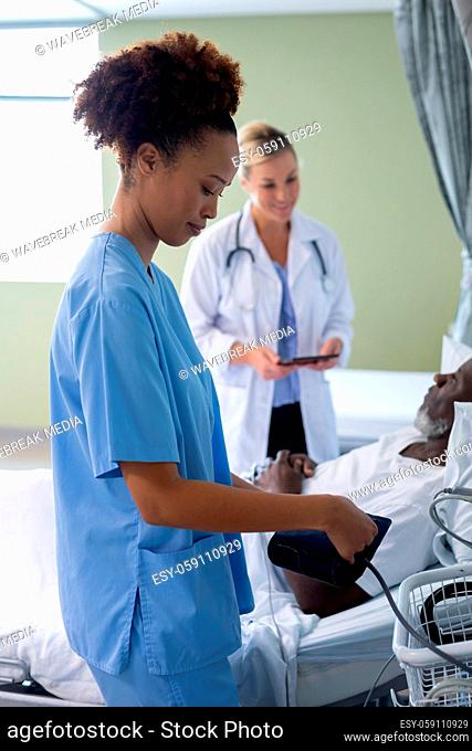 Mixed race female doctor in patient room preparing to checking blood pressure of male patient