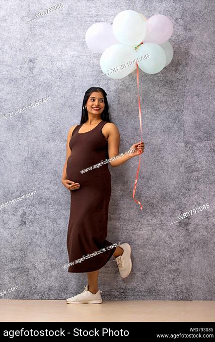 Pregnant woman standing against wall with a bunch of balloons
