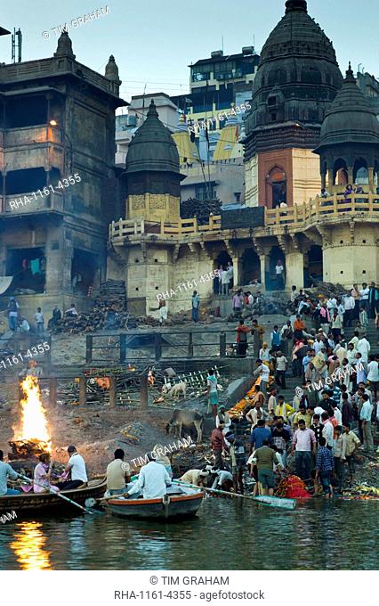 Tourists watch body bathed in River Ganges and traditional Hindu cremation on funeral pyre at Manikarnika Ghat in Holy City of Varanasi, Benares, India