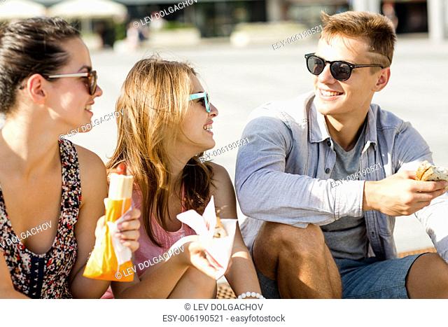 friendship, leisure, summer and people concept - group of smiling friends in sunglasses sitting with food on city square