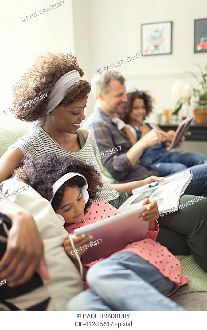 Multi-ethnic young family relaxing, reading and using digital tablet on sofa