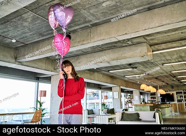 Businesswoman holding balloons while standing in loft office