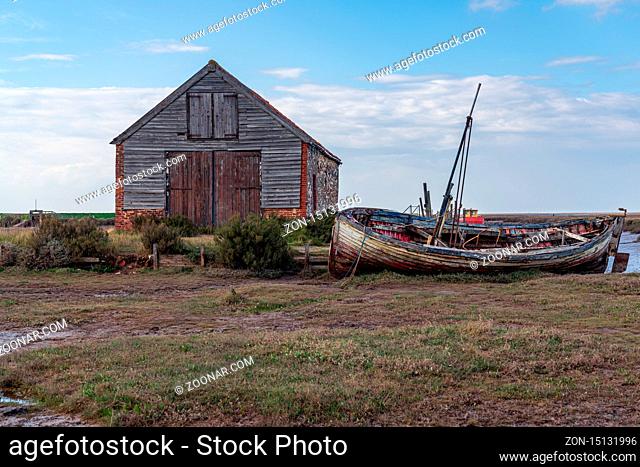 Thornham, Norfolk, England, UK - April 24, 2019: An old stone barn in Thornham Old Harbour with a wooden sailing boat next to it