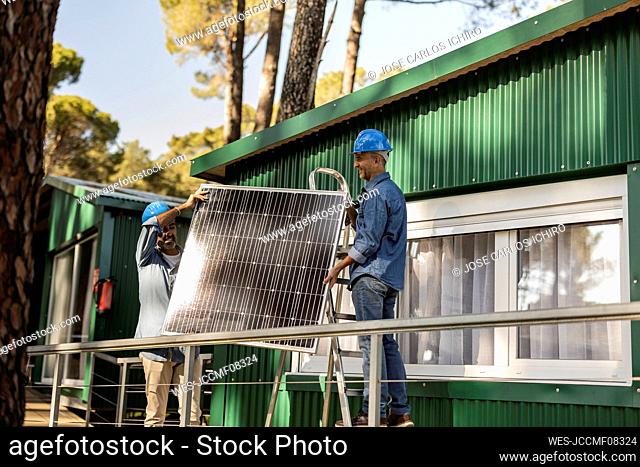 Photovoltaic technicians mounting solar panel on sustainable house