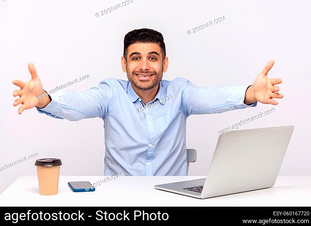 Come into my arms. Excited happy friendly businessman sitting office workplace, stretching hands to camera, going to embrace, welcoming on reception