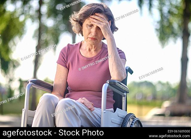 Unhappy. Disabled mid aged woman sitting in a wheel-chair with an unhappy look