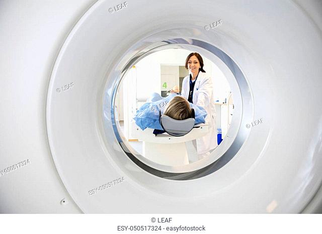Smiling doctor looking at patient undergoing CT scan in hospital